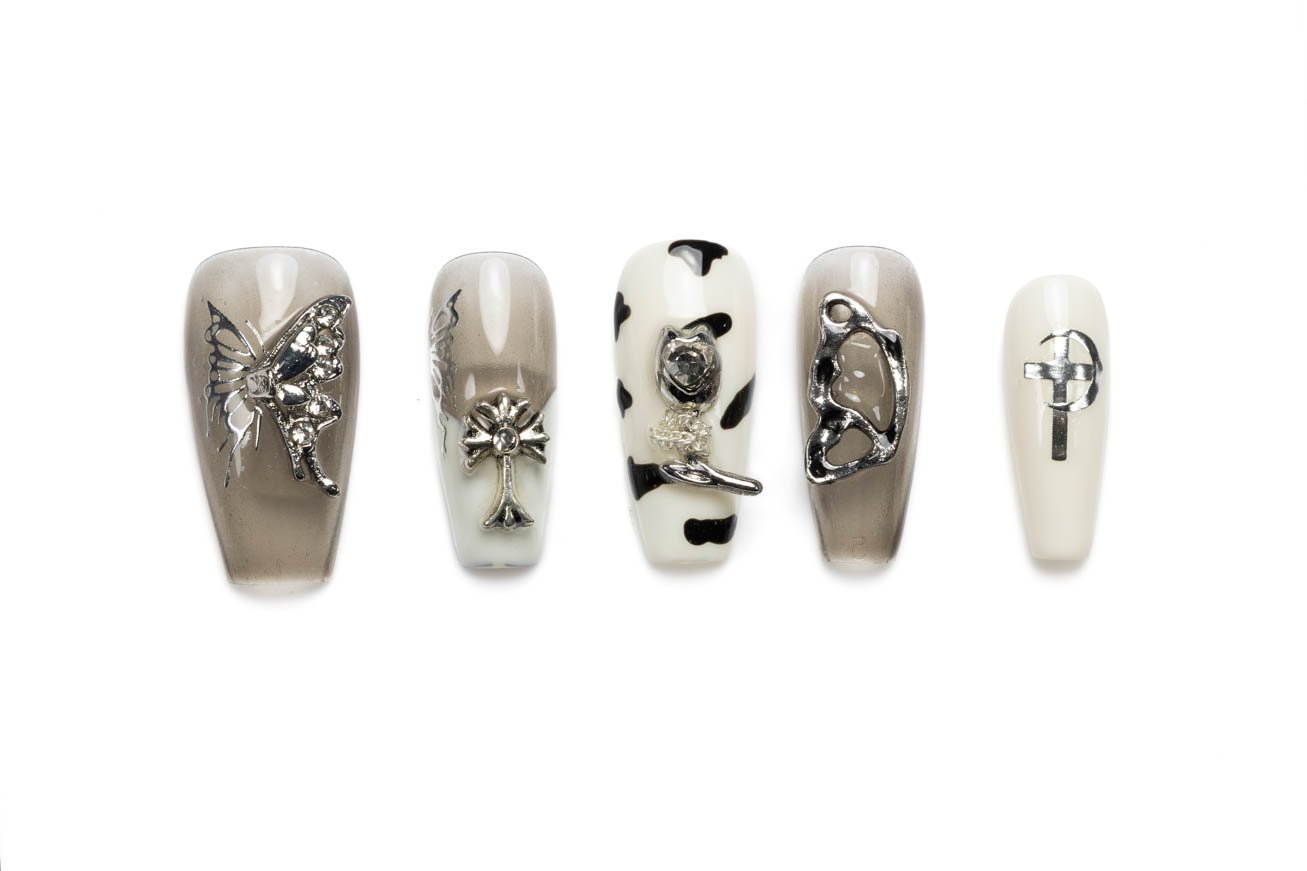 Taupe and white coffin press-on nails with butterfly charms, cross accents, and cow print design details