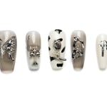 Taupe and white coffin press-on nails with butterfly charms, cross accents, and cow print design details