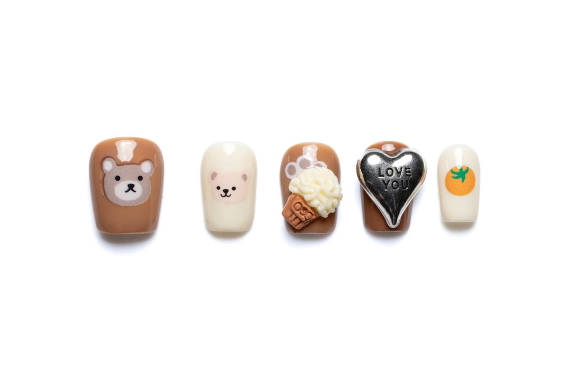 Short squoval press-on nails with cute bear faces, ice cream cone, love heart, and persimmon designs in warm brown and orange tones