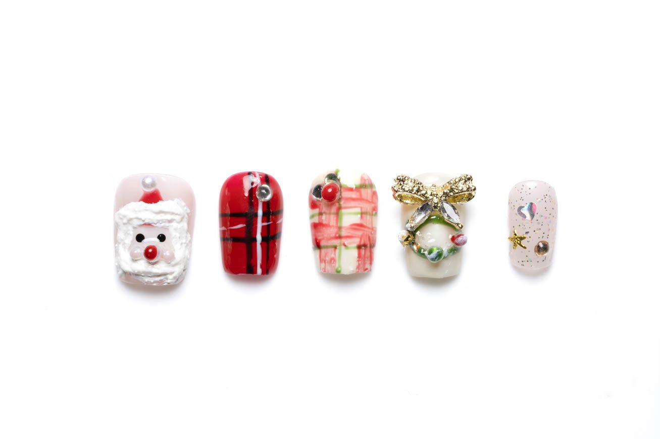 Christmas-themed coffin press-on nails featuring Santa face design, red plaid pattern, crystal-adorned 3D bow, and festive glitter embellishments