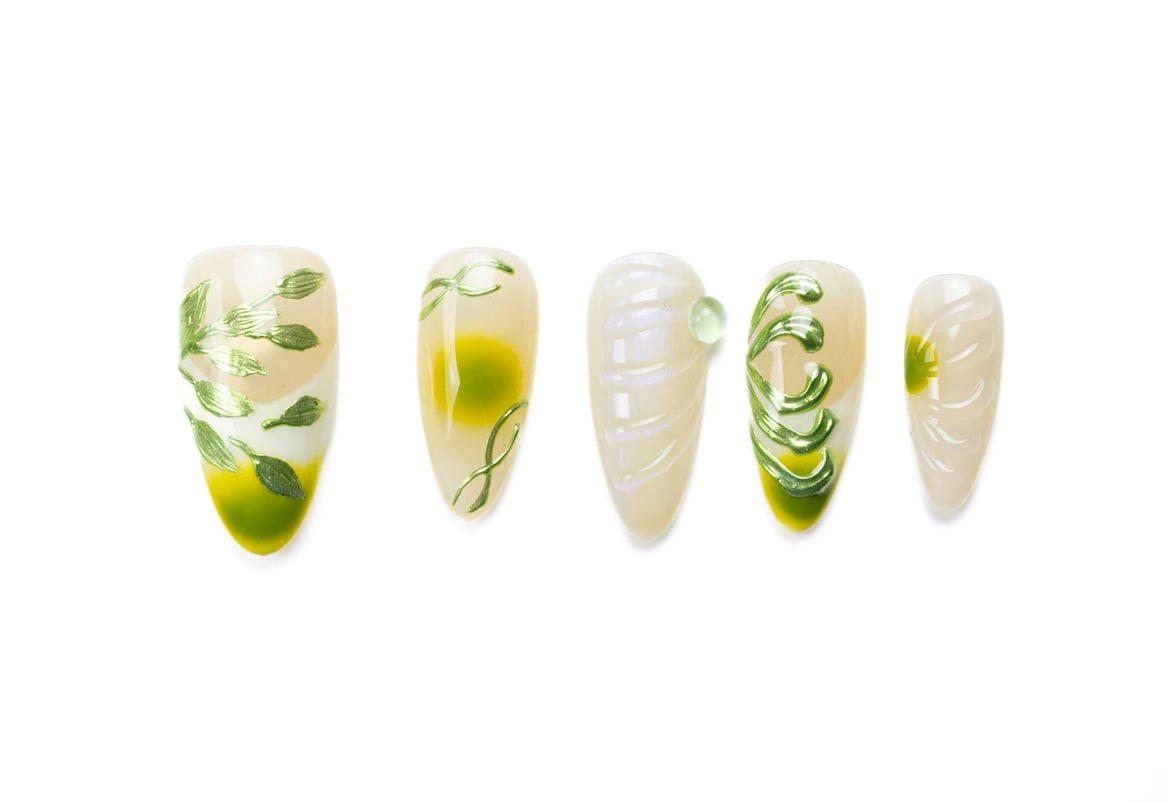 Almond-shaped press-on nails with green French tips and leaf designs on neutral base, featuring metallic accents and swirls