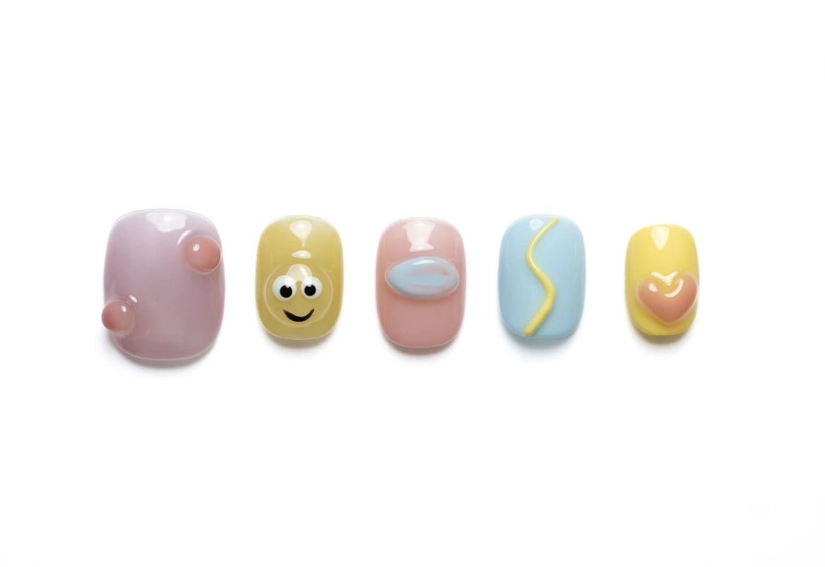 Short round press-on nails in pastel colors with 3D hearts, smiley faces, and colorful dots, perfect for a cute everyday manicure