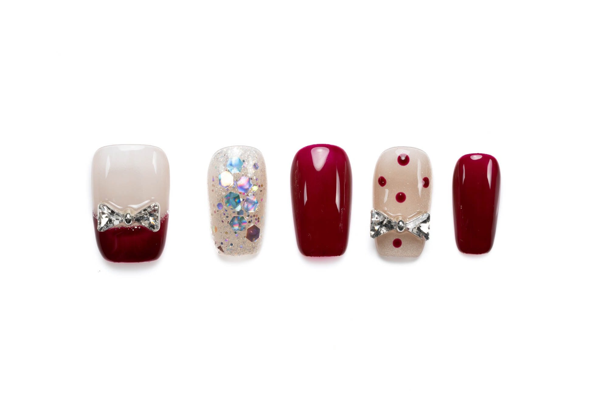 Short coffin press-on nails in burgundy and nude with sparkly rhinestone bow accents, glitter, and polka dot details