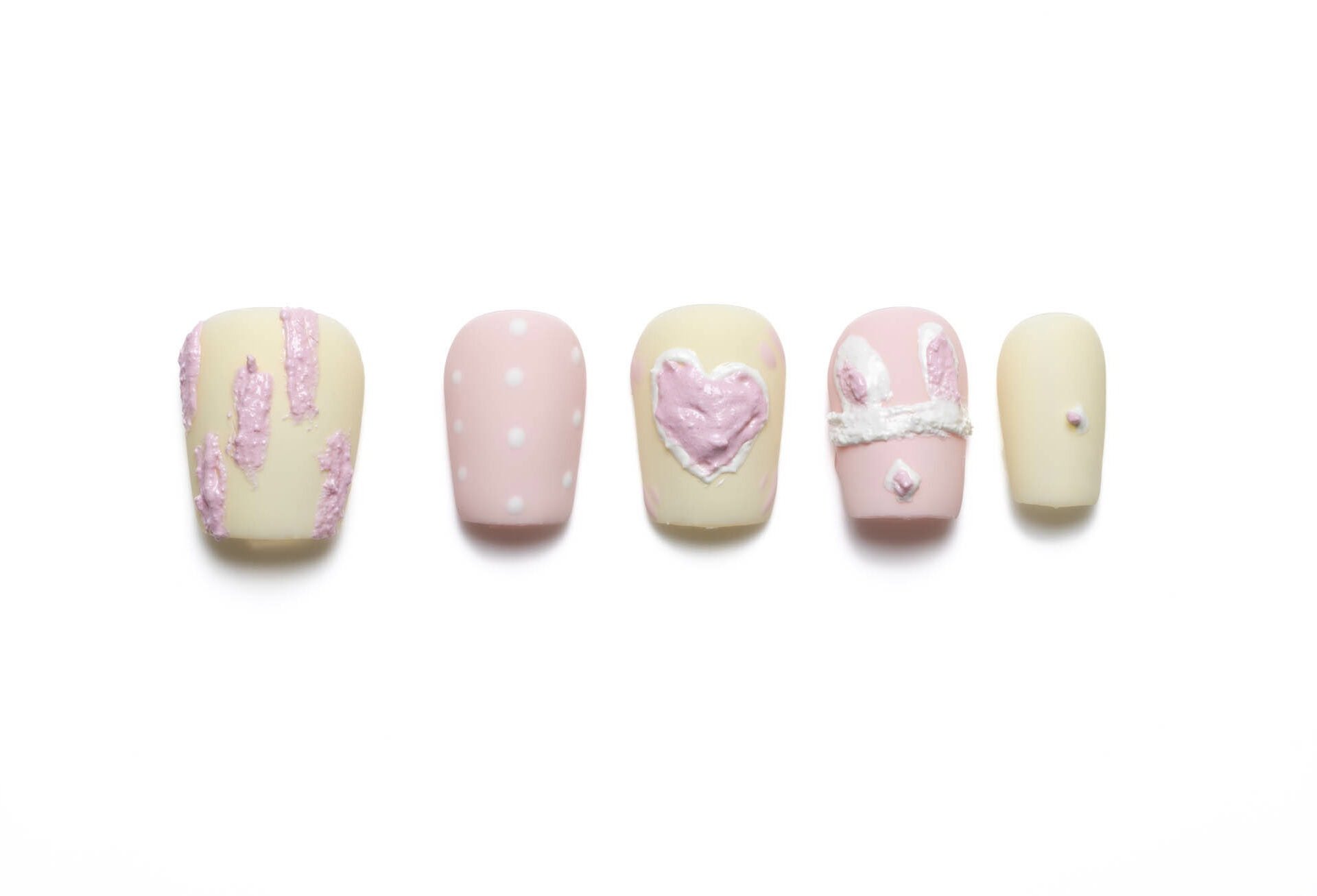 Short squoval press-on nails with pink and cream bunny theme, featuring polka dots, 3D hearts, and decorative bunny ear designs