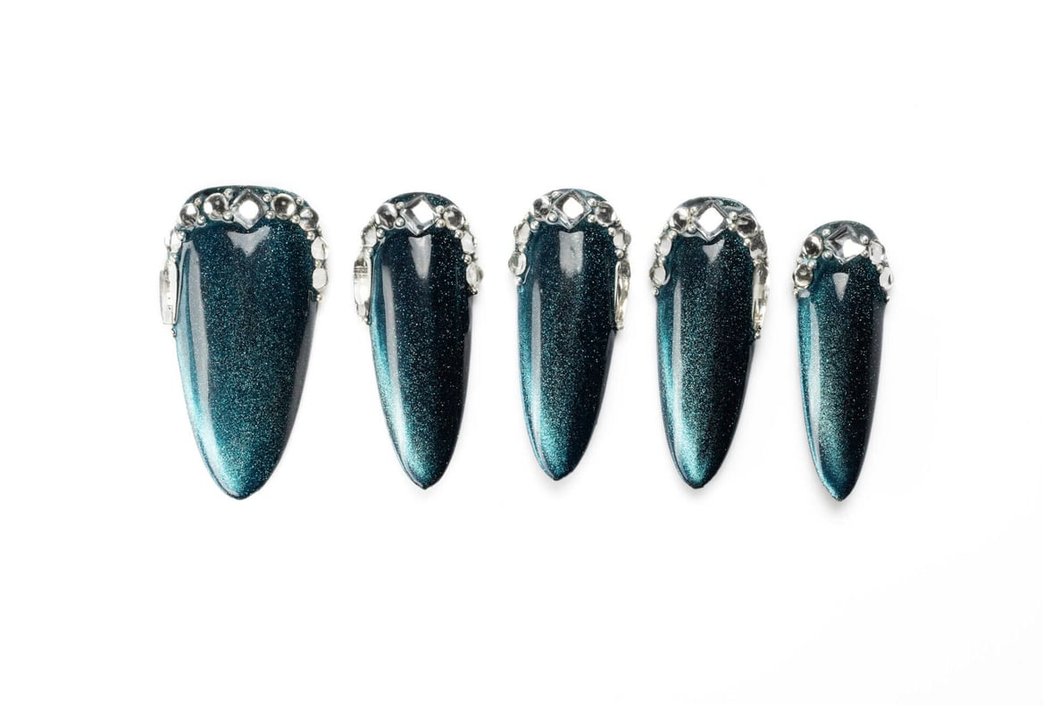 Dark teal stiletto press-on nails with shimmering cat eye effect and crystal border detail, showing dramatic length and shine