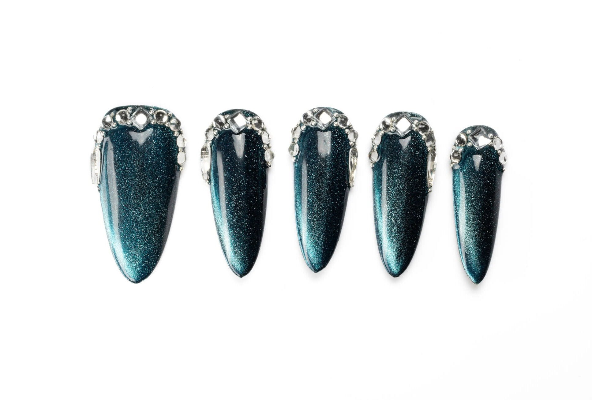 Dark teal stiletto press-on nails with shimmering cat eye effect and crystal border detail, showing dramatic length and shine