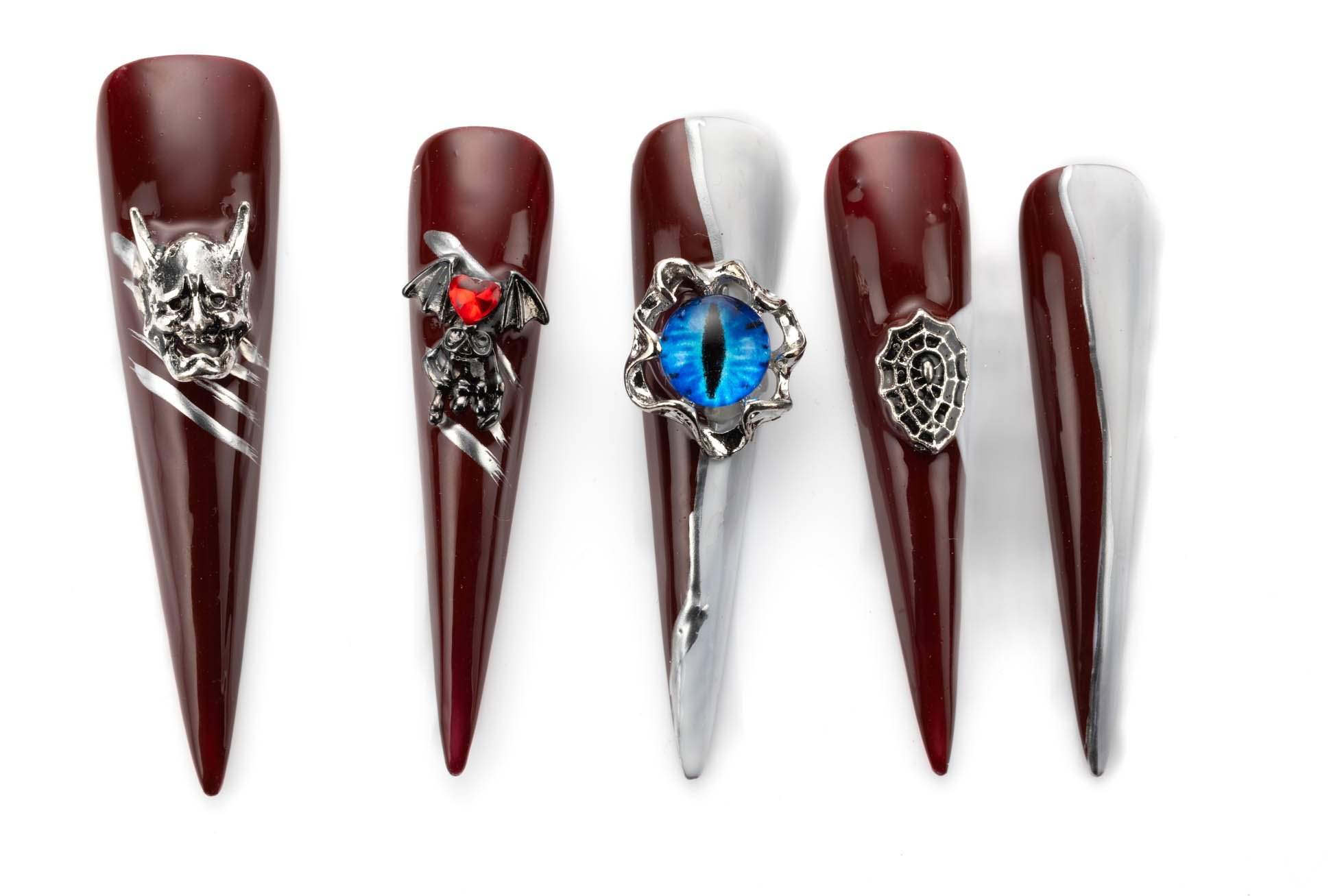 Long stiletto press-on nails in deep red and silver with gothic designs including oni mask, bat, evil eye, and spiderweb embellishments