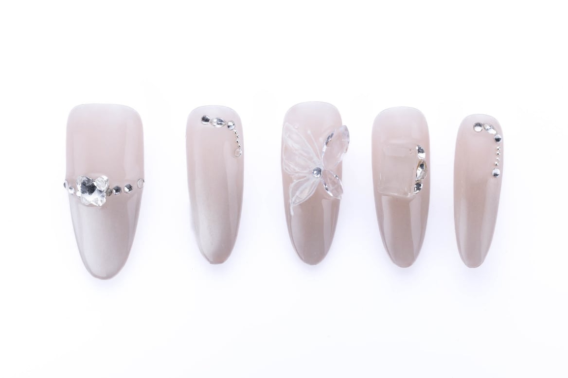 Almond-shaped press-on nails in a sheer nude shade with a 3D butterfly accent and sparkling rhinestones, creating a delicate and whimsical look.