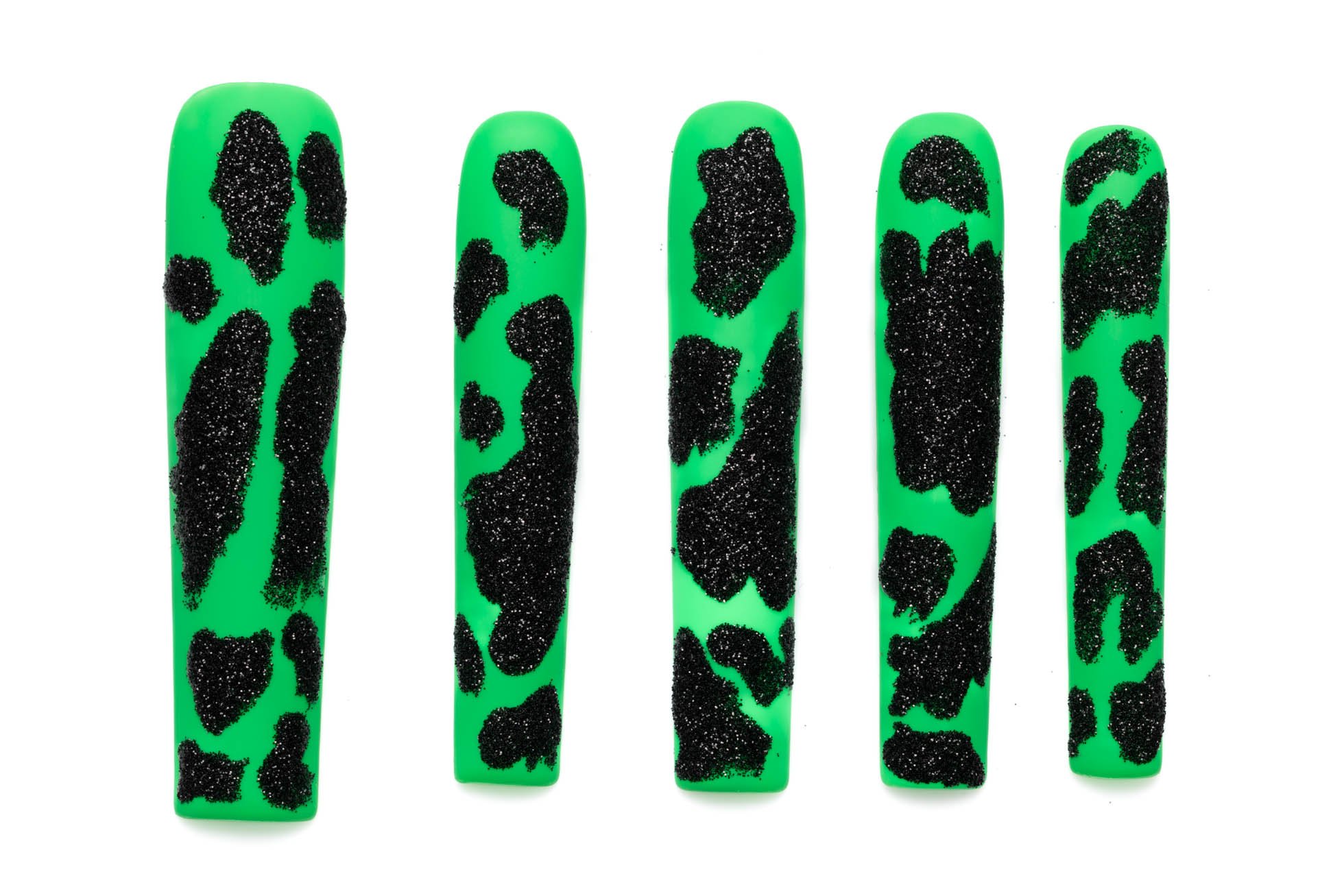 Extra long coffin press-on nails in bright green with sparkly black cow print pattern, arranged in descending size order