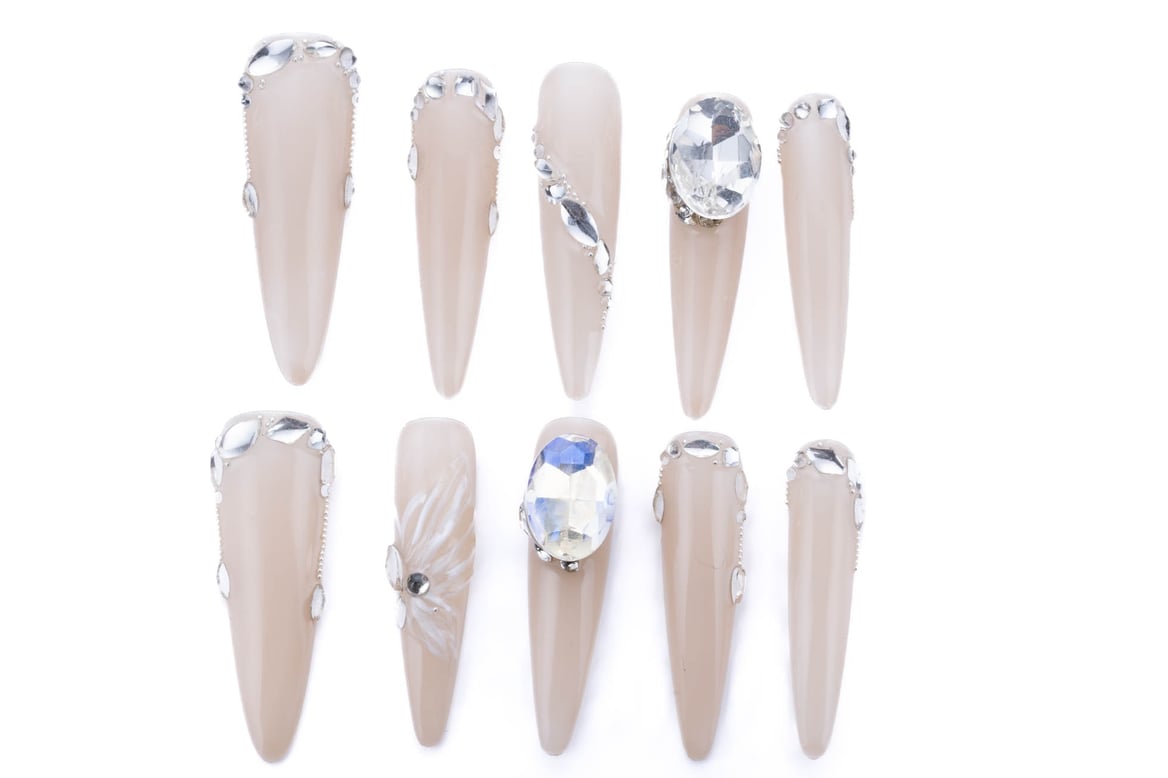 Luxury bridal press-on nails with a soft nude base, almond shape, and various sparkling rhinestone embellishments for a glamorous wedding look.