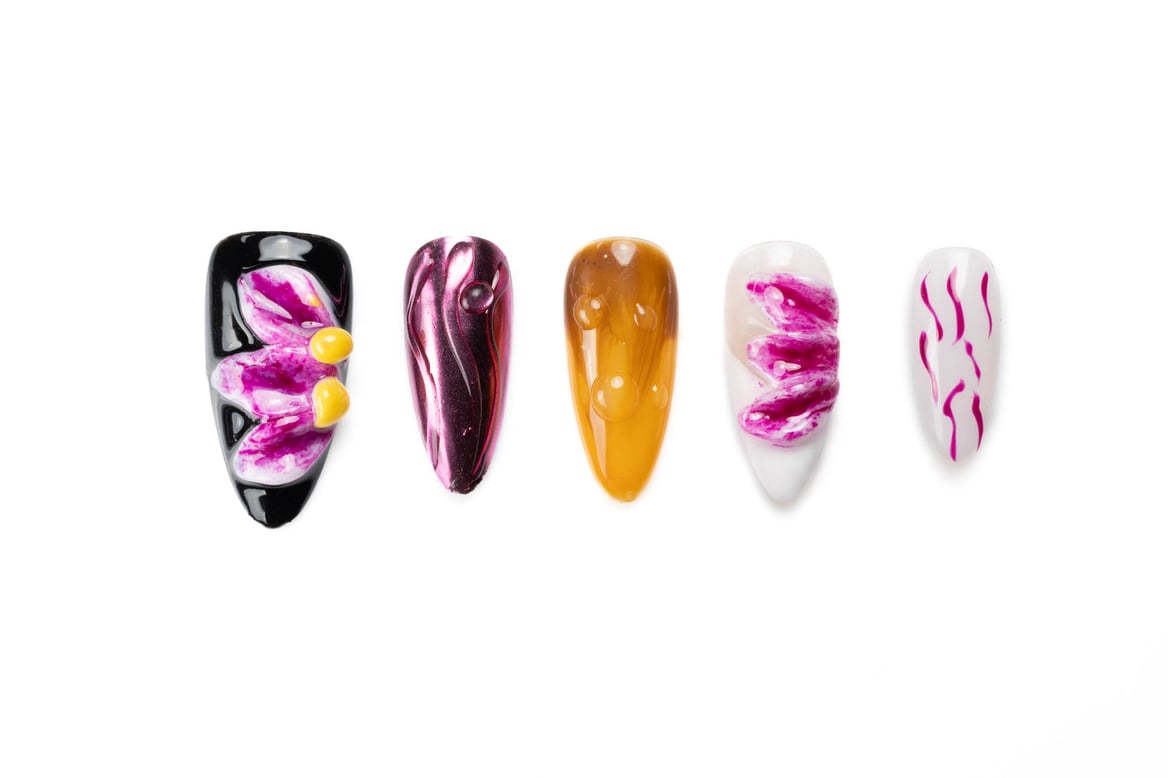 Artistic almond-shaped press-on nails with vibrant floral designs in pink, yellow, and black with swirl patterns